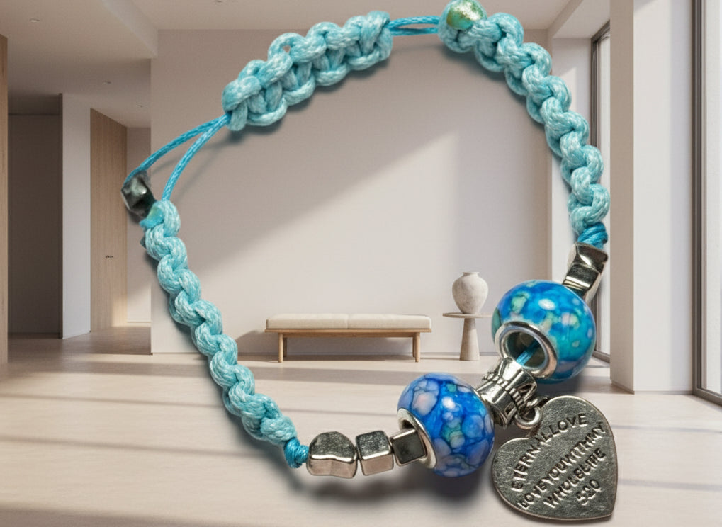 Blue braided bracelet with decorative beads and a heart-shaped tag on a neutral background
