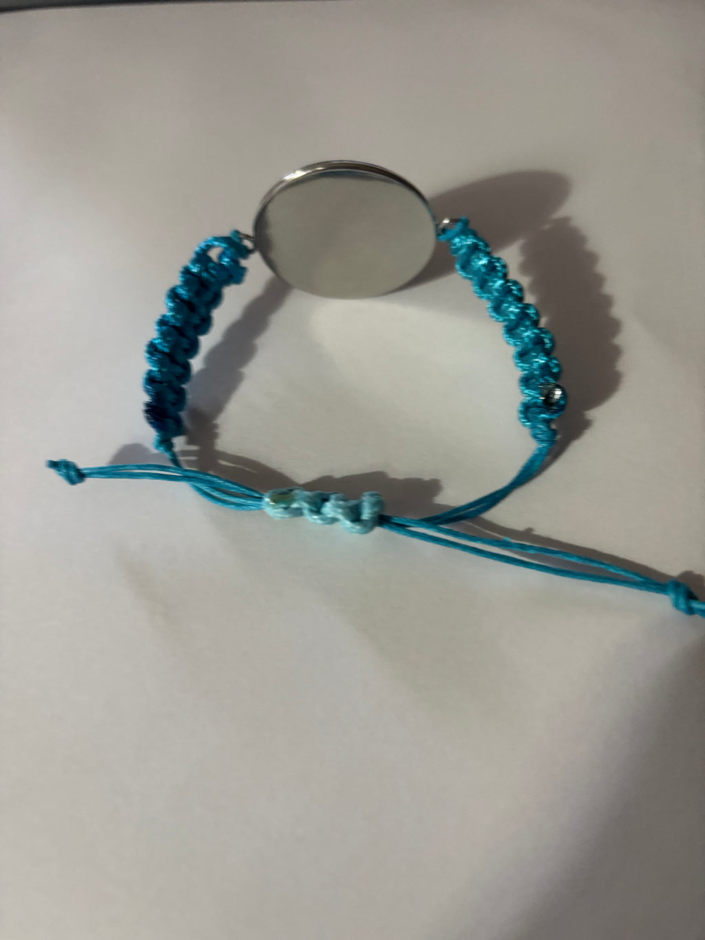 Blue braided bracelet with a round silver charm on a white background