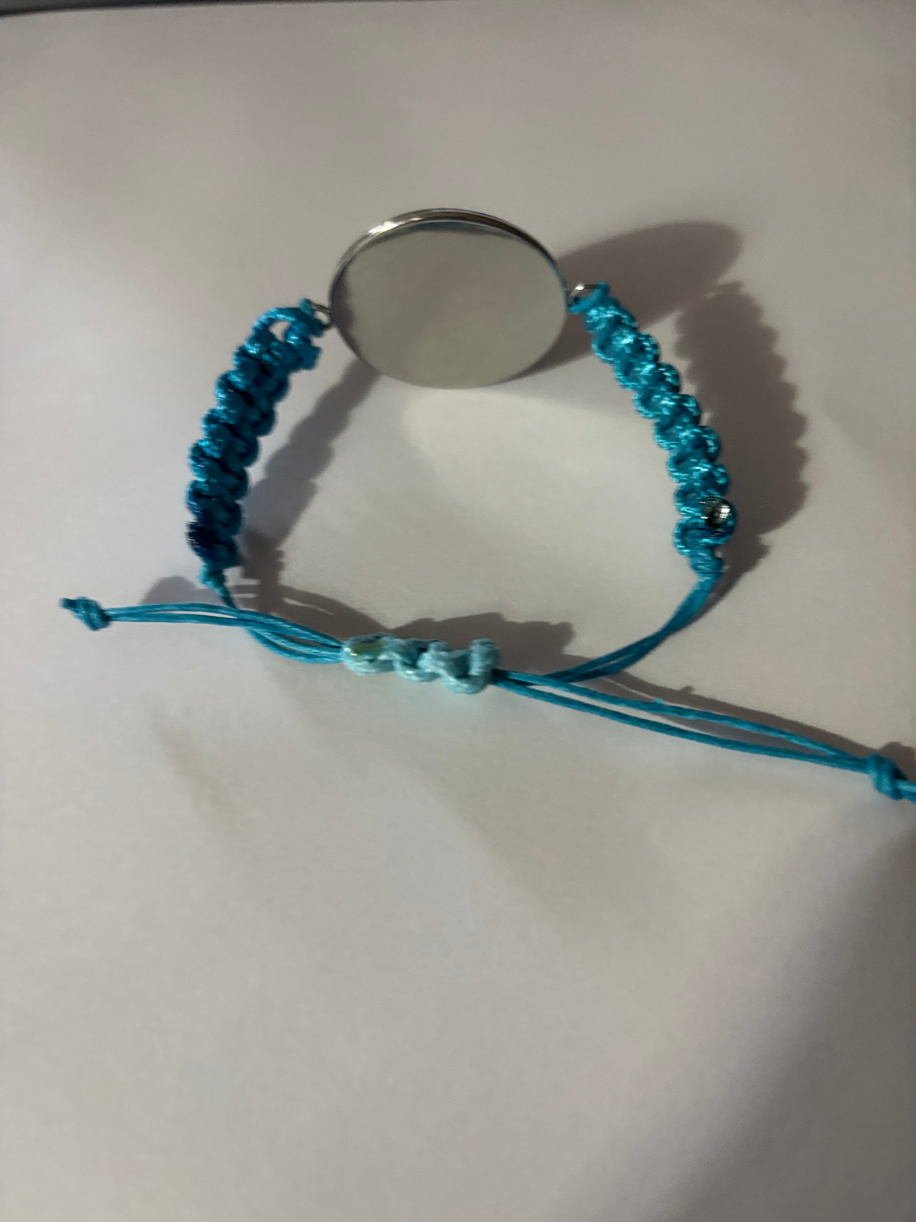 Blue braided bracelet with a round silver charm on a white background