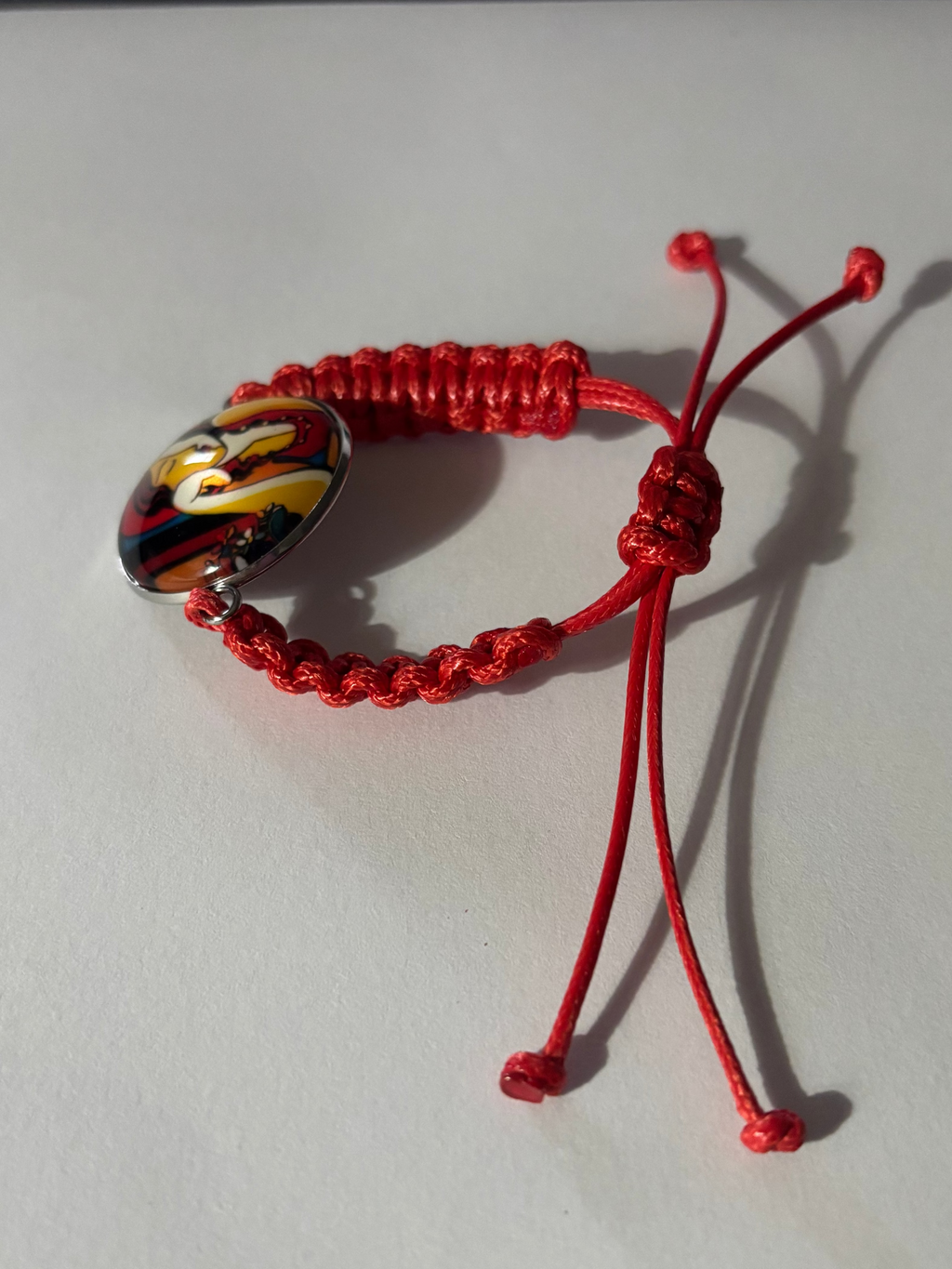 Red braided bracelet with a colorful charm on a white background