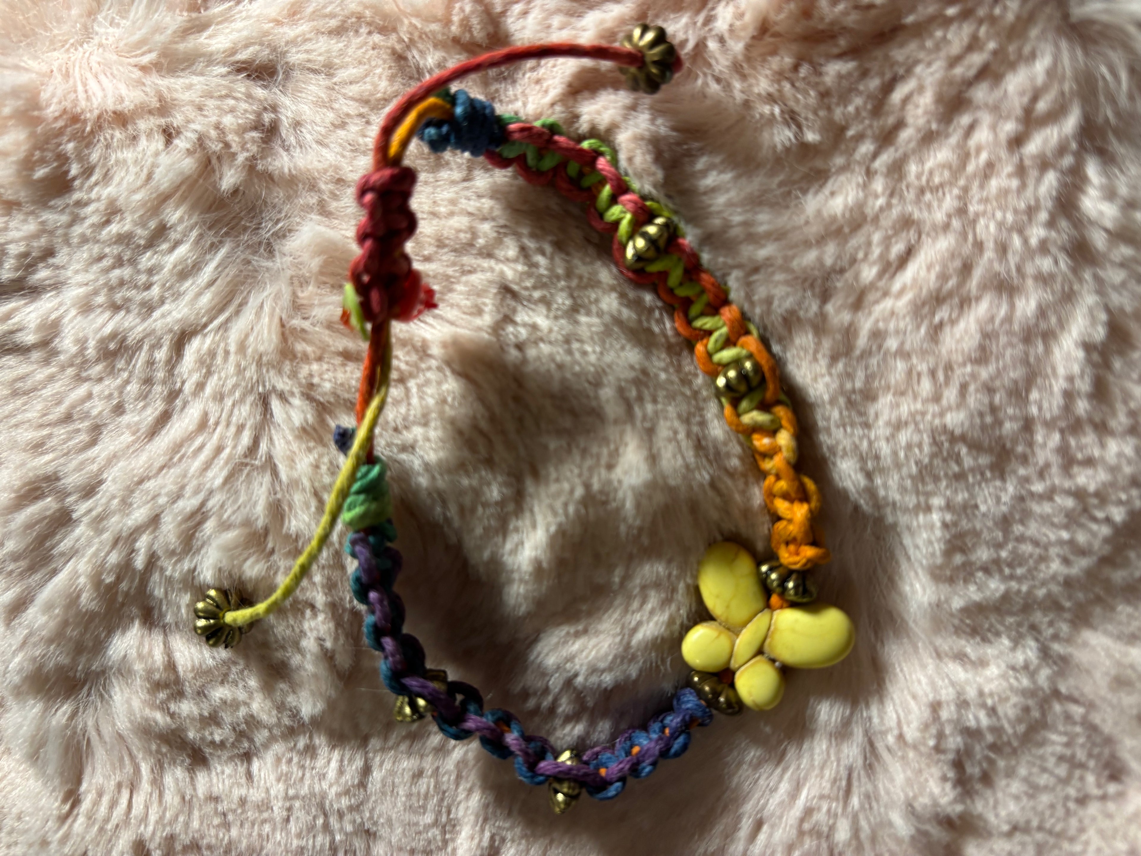 Colorful braided bracelet with beads and a yellow flower charm on a soft pink background