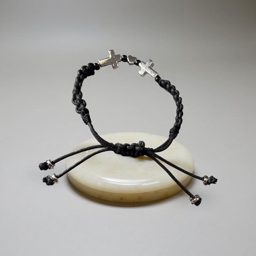 Black braided bracelet with silver cross charms on a light gray background