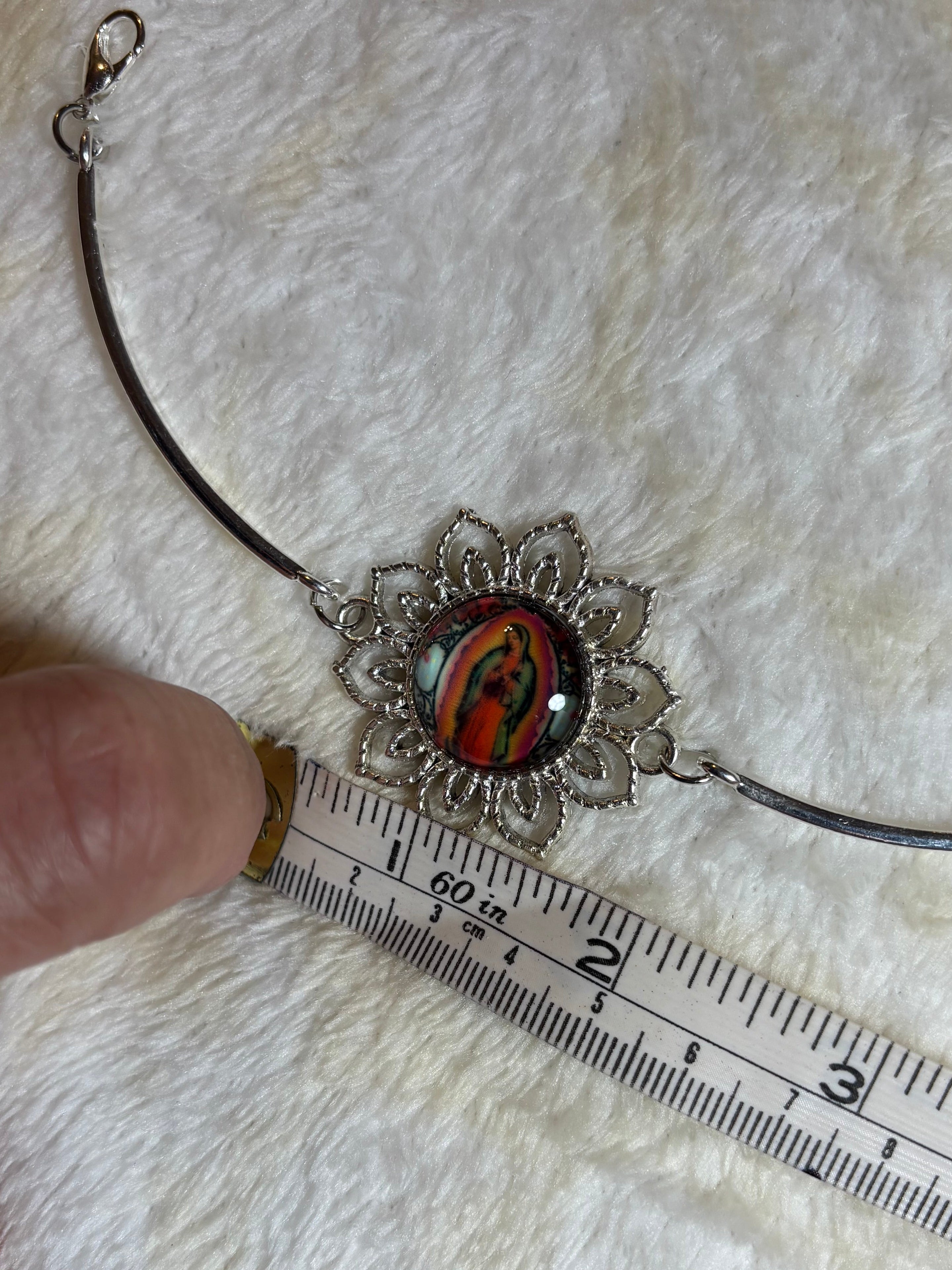 Necklace with a decorative pendant being measured against a ruler on a textured surface.