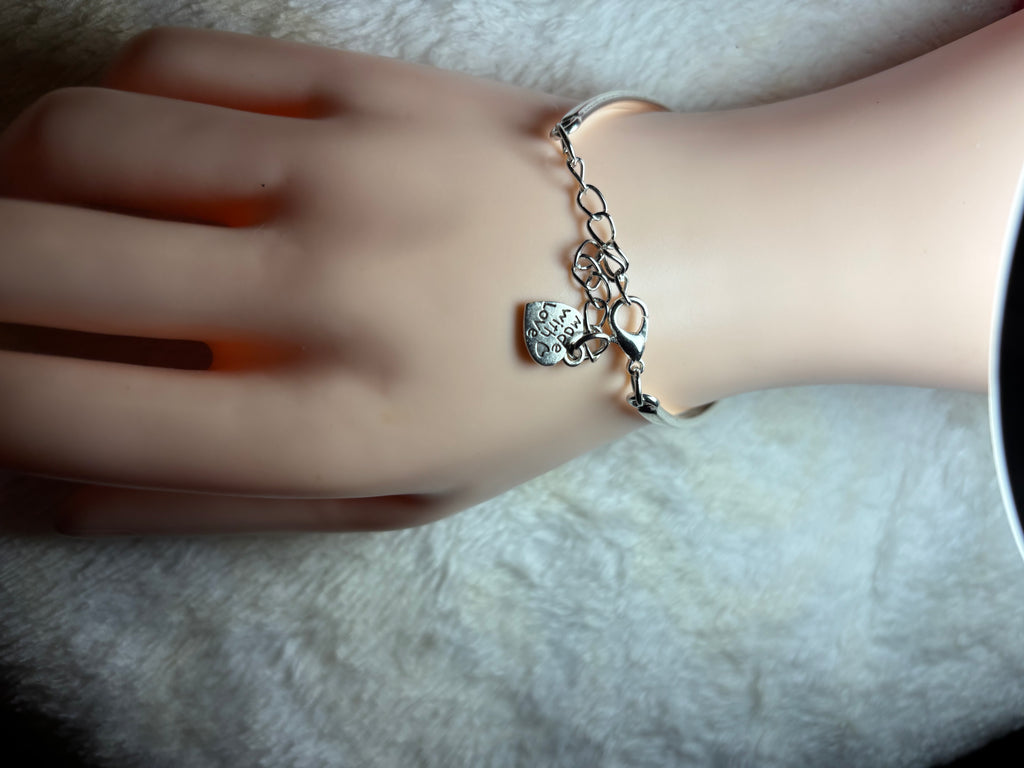 Hand wearing a silver bracelet with a heart charm on a neutral background