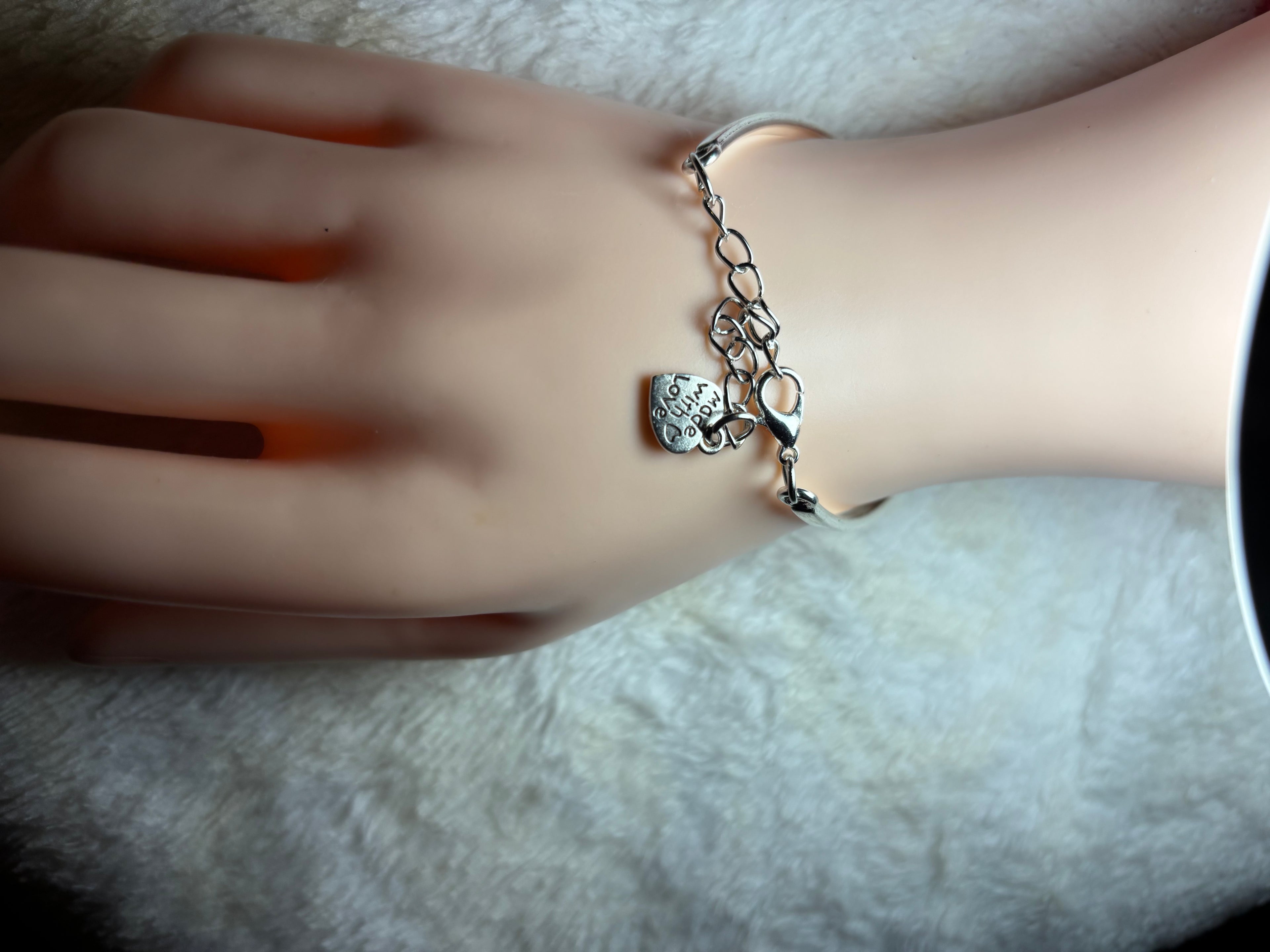 Hand wearing a silver bracelet with a heart charm on a neutral background