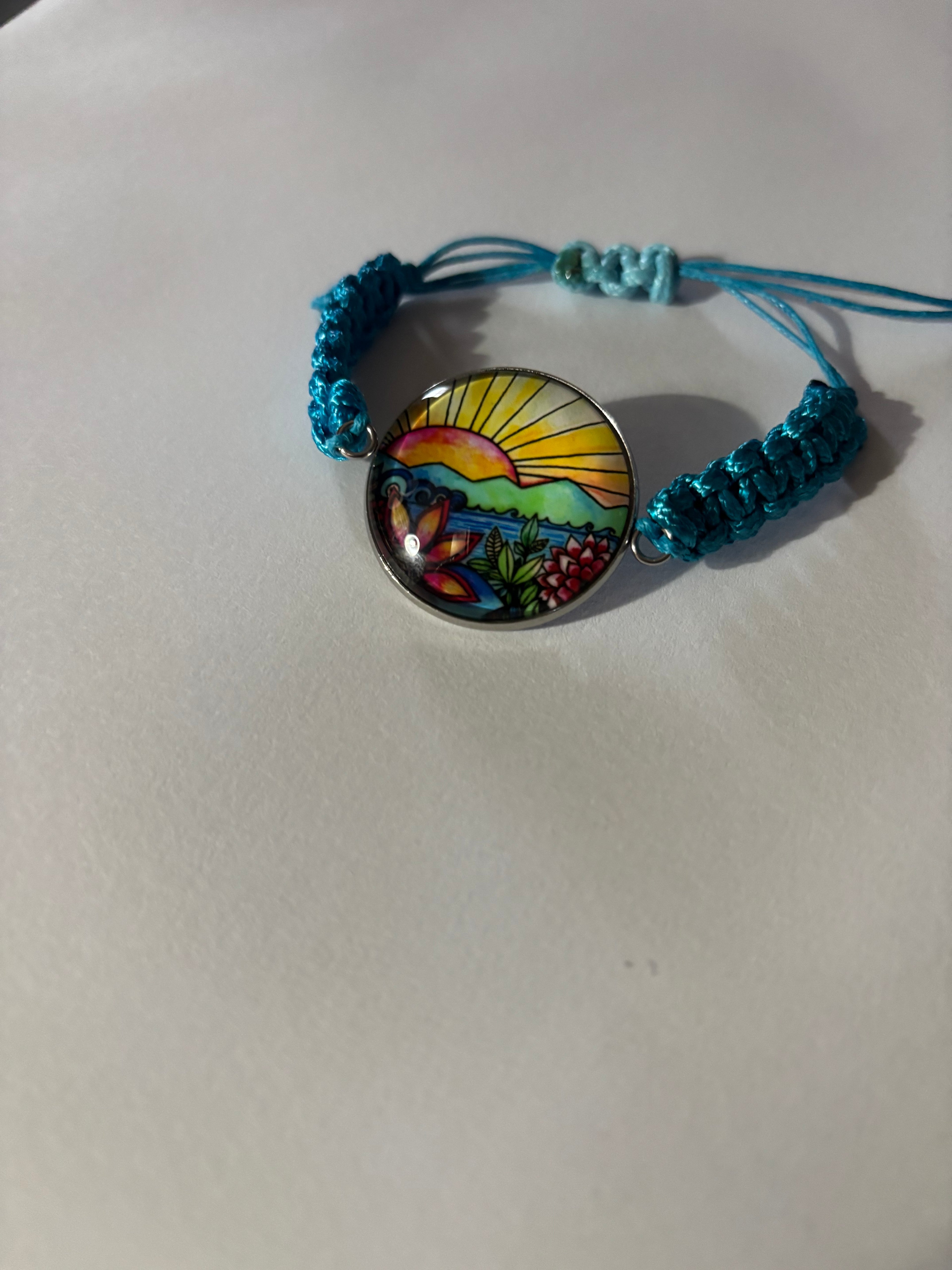Turquoise braided bracelet with a colorful circular charm on a light gray background